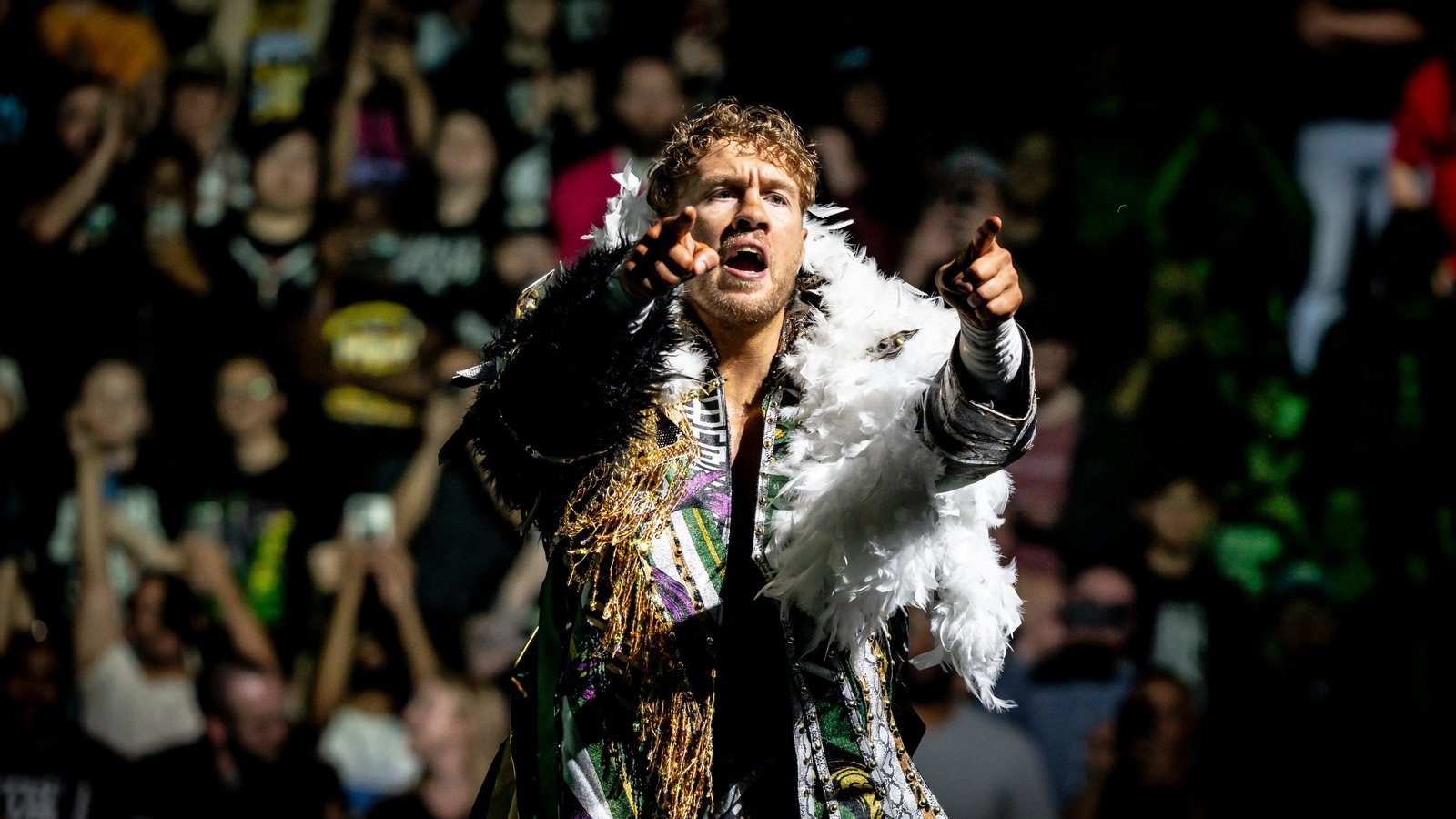 Will Ospreay in a feathered entrance jacket pointing at the crowd during his entrance at AEW Revolution 2024