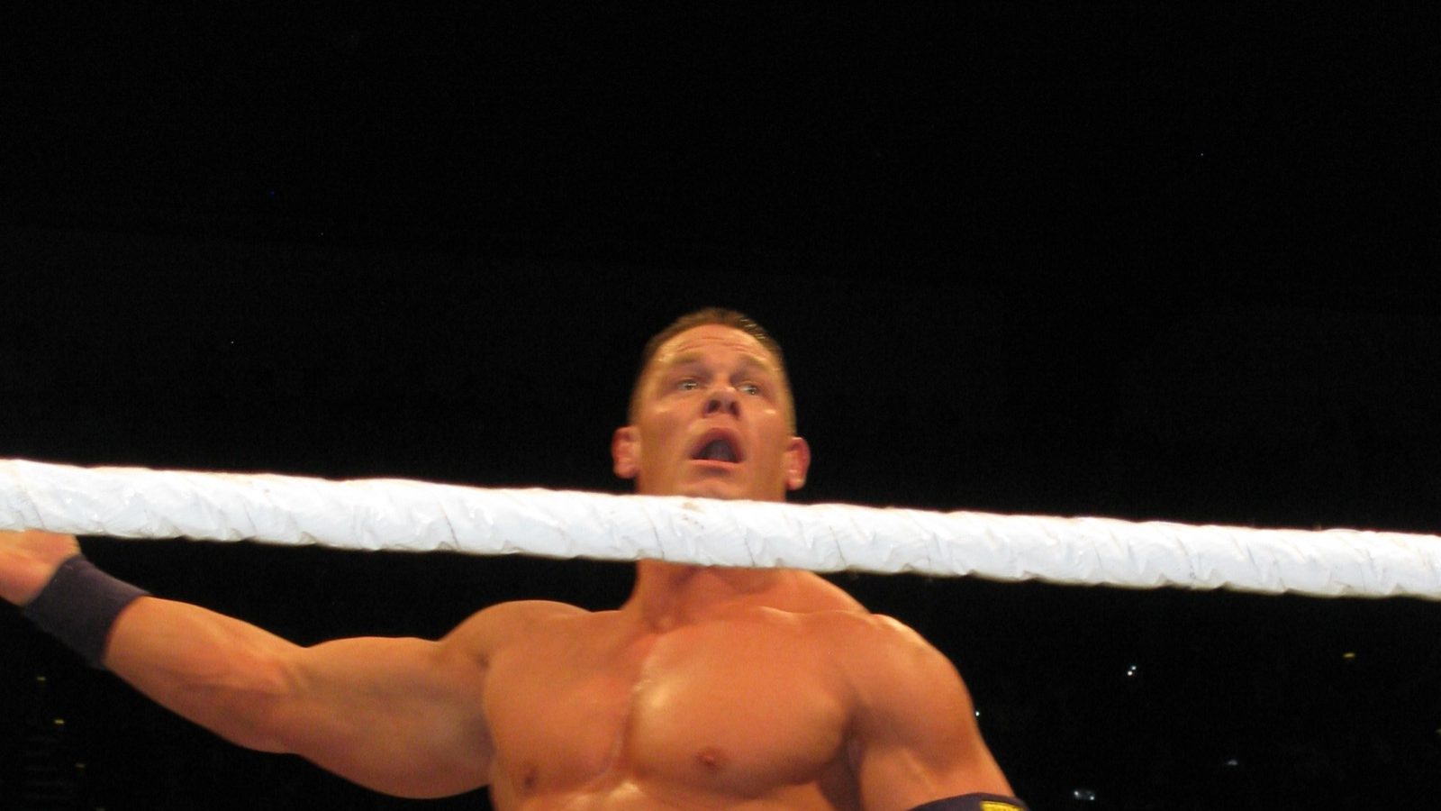 John Cena standing in the ring behind the ropes with a championship belt in his hand at a WWE house show in Adelaide in 2013