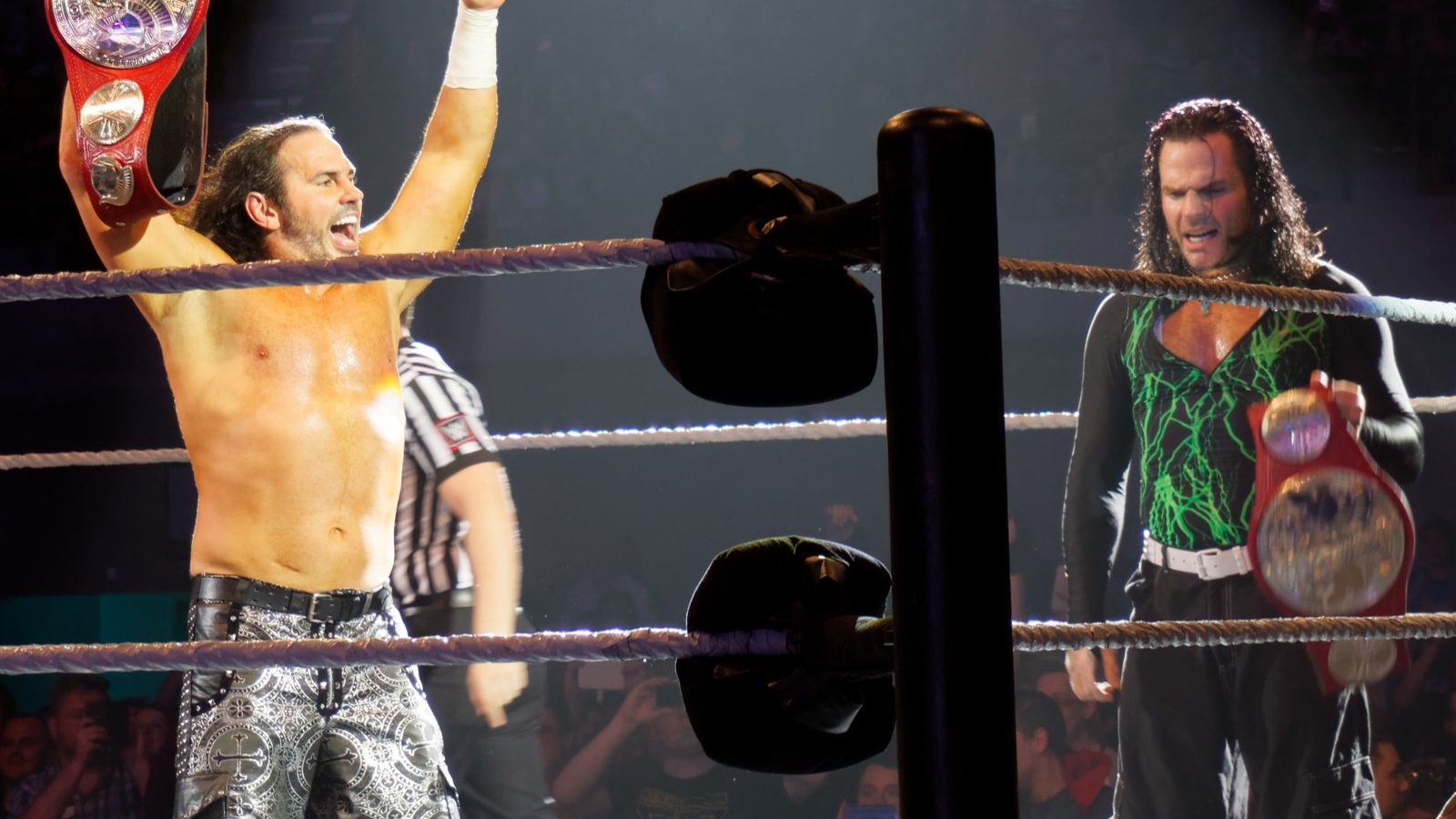 Matt Hardy raising a fist and Jeff Hardy holding tag team title belts in the ring at a WWE event in 2017