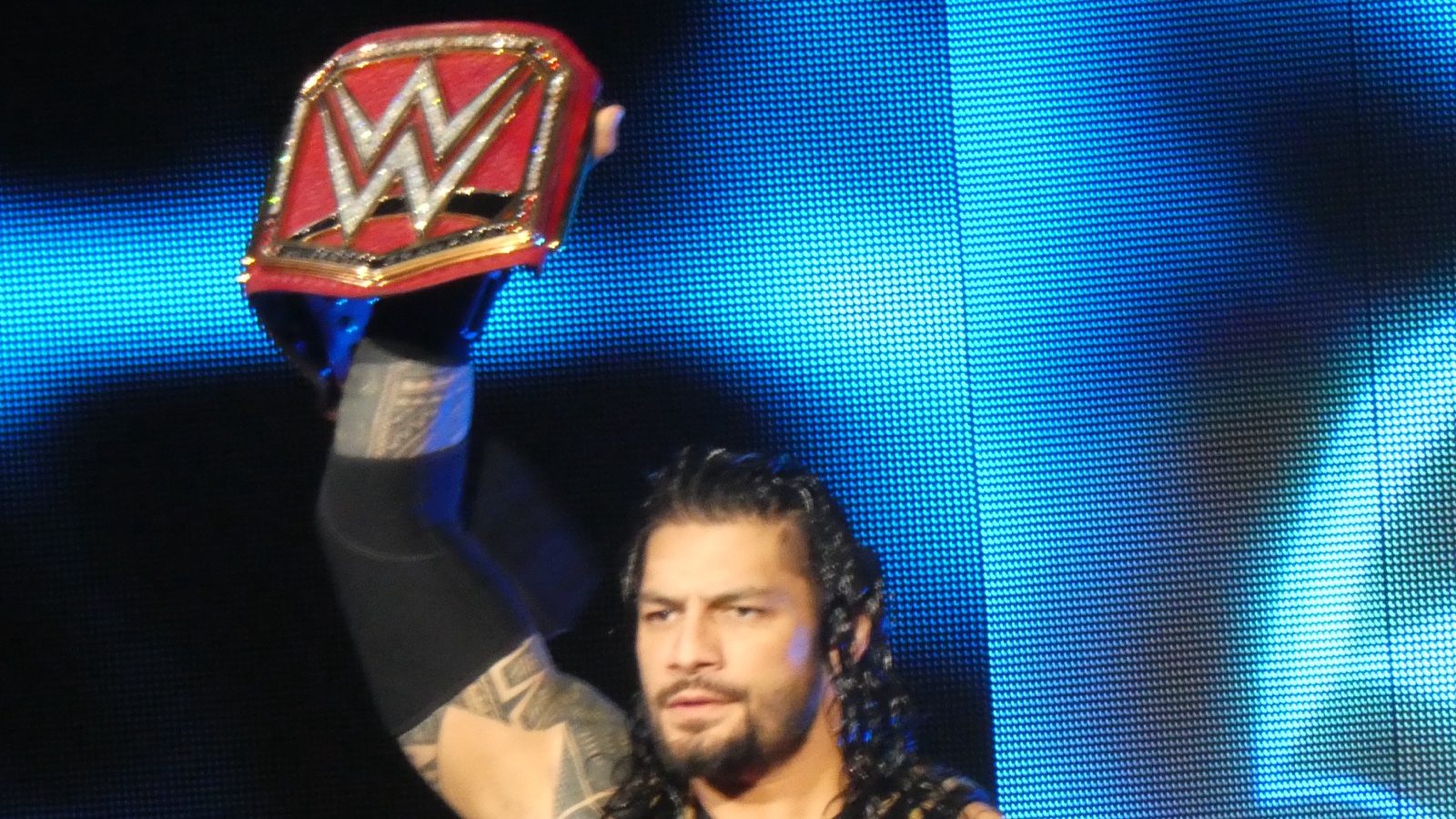 Roman Reigns holding a championship belt above his head during his entrance